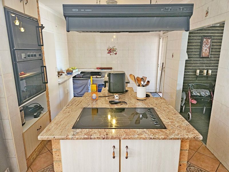 A functional kitchen featuring a central granite island with a built-in hob, double wall oven, and tiled finishes throughout.