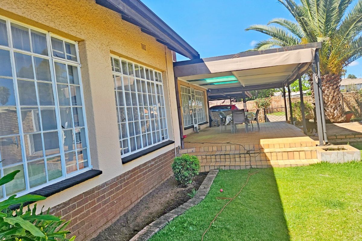 Rear view of the property featuring a covered patio area, brick and plaster facade, and a well-maintained garden space.