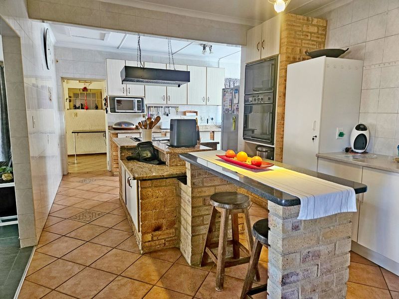 A spacious kitchen featuring a brick-built island with a breakfast bar, integrated double oven, and tiled finishes throughout.