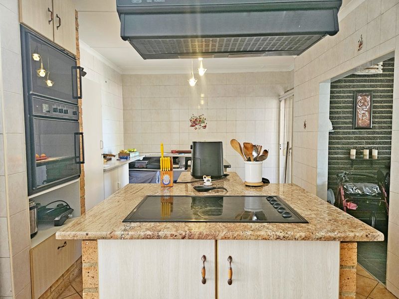 A functional kitchen featuring a central island with a built-in electric hob, granite countertops, and integrated oven cabinetry.