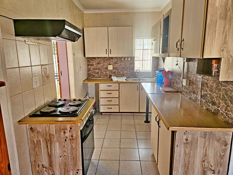 A functional kitchen featuring built-in cabinetry, laminate countertops, an electric hob with extractor fan, and tiled finishes throughout.