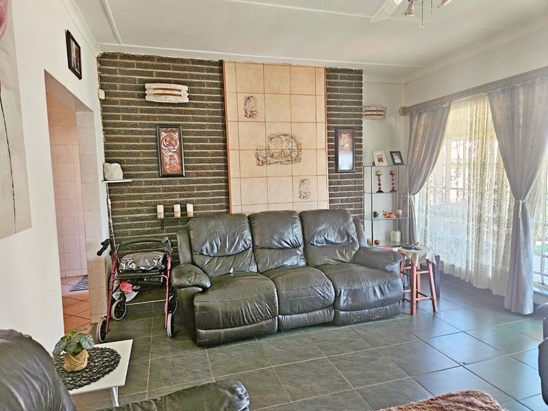 A living room featuring an exposed brick wall with a central tiled panel, ceramic floor tiles, and a ceiling fan.