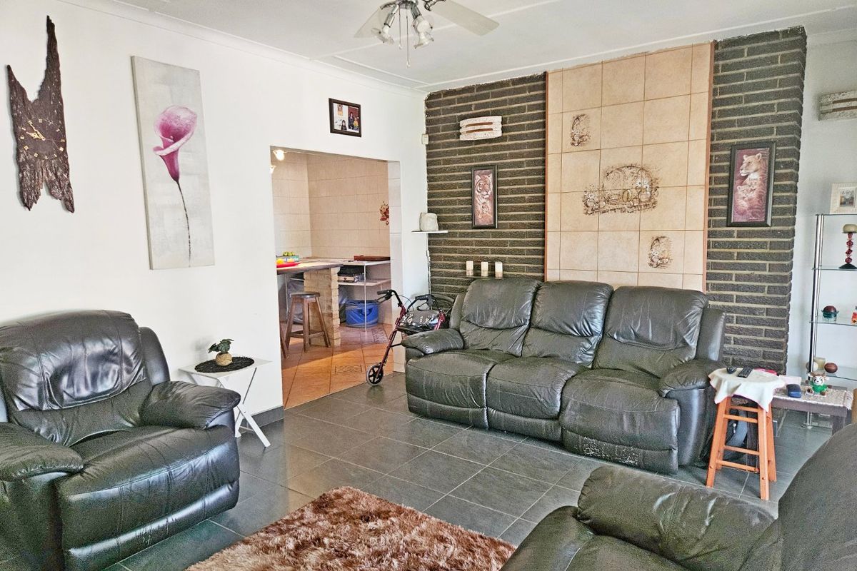Spacious living room featuring dark tiled flooring and a prominent exposed brick feature wall, with an open-plan flow into the adjacent kitchen area.