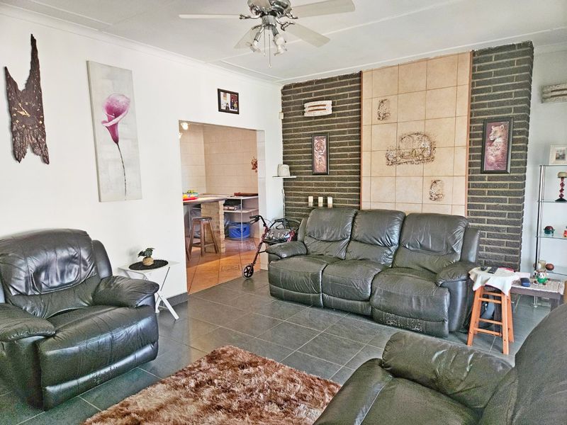 Spacious living room featuring dark tiled flooring and a prominent exposed brick feature wall, with an open-plan flow into the adjacent kitchen area.