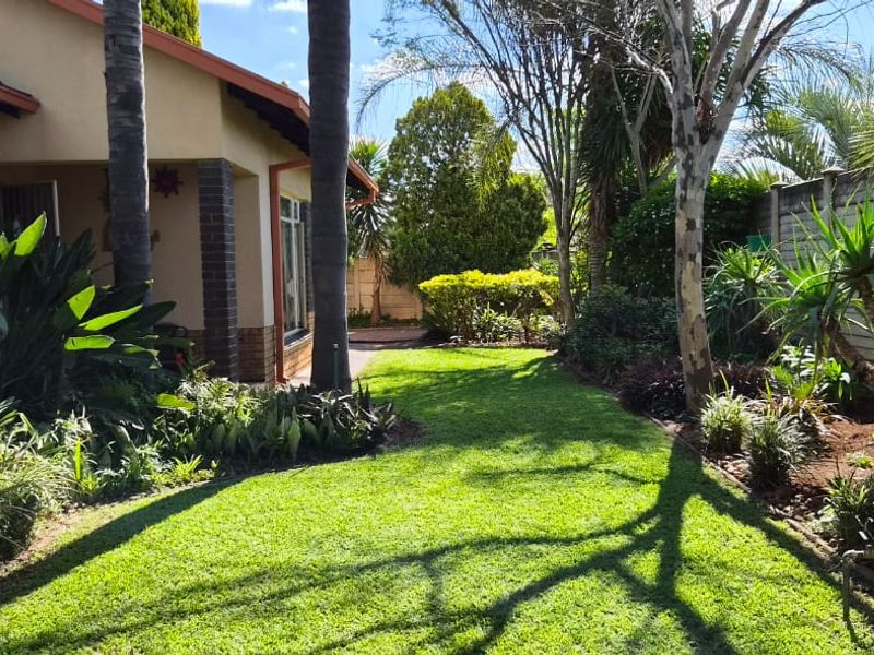 A well-maintained rear garden featuring a lush lawn, mature trees, and a secure precast concrete boundary wall adjacent to the house exterior.