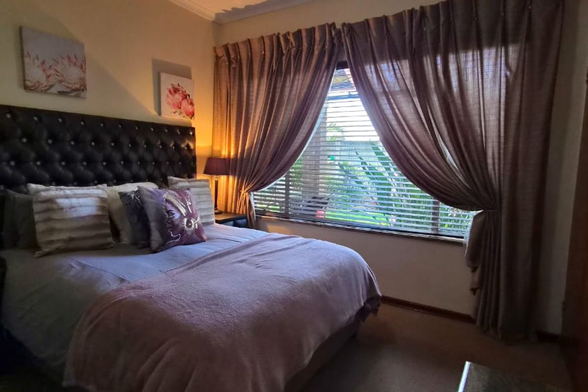 A cozy bedroom featuring a large window with blinds and curtains, and a built-in cupboard for storage.