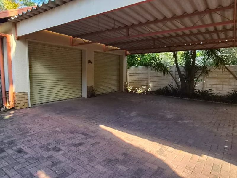 A spacious double garage with an attached covered carport and paved driveway, featuring secure brick boundary walls.