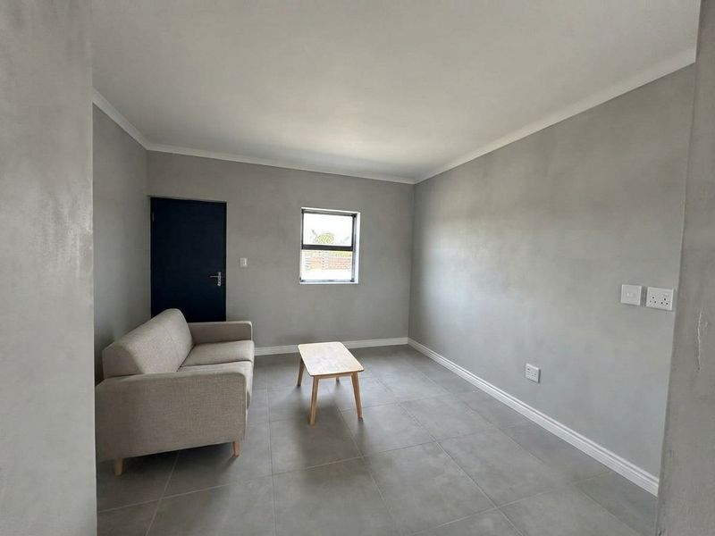 A minimalist living room featuring neutral grey walls, large format floor tiles, and clean white trim finishes.