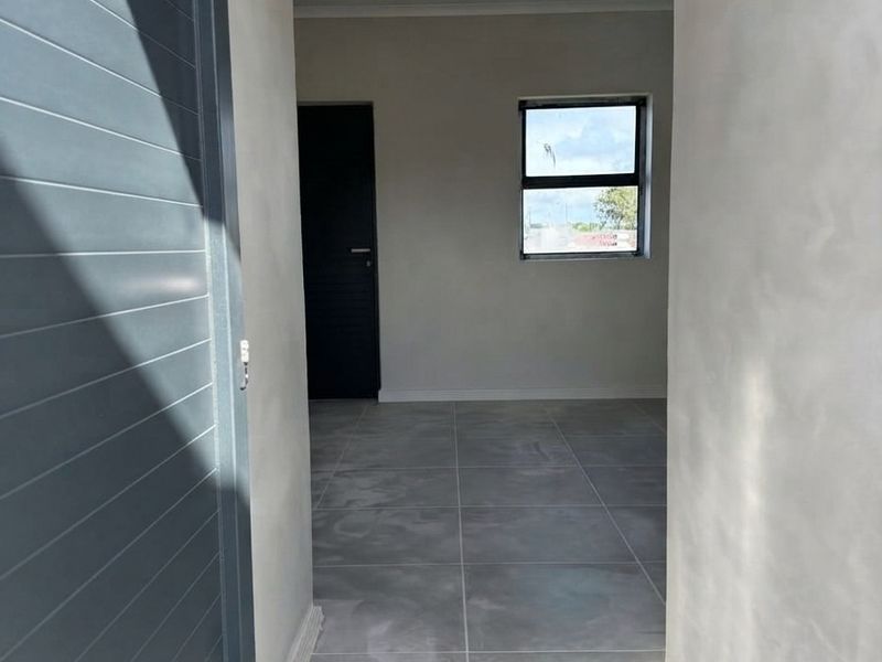 A bright, empty hallway featuring modern grey floor tiles, recessed downlighting, and a clean, neutral finish throughout.