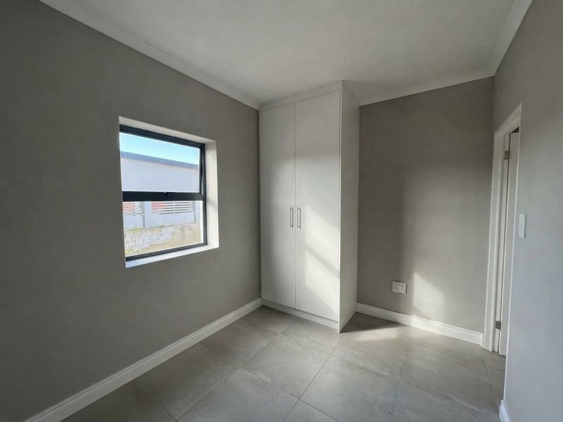 A clean, empty bedroom featuring neutral grey walls, tiled flooring, and a modern built-in wardrobe with white cabinetry.