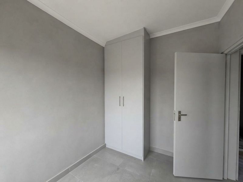 A clean, neutral bedroom featuring modern tiled flooring, built-in cupboards, and crisp finishes, ready for personalization.