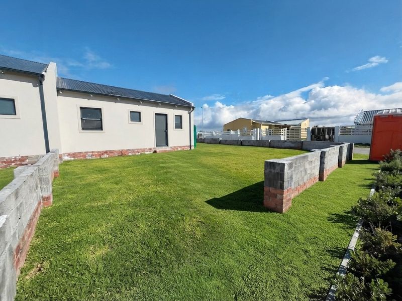A rear garden area featuring a lawn and partially constructed concrete block boundary walls adjacent to the main dwelling structure.