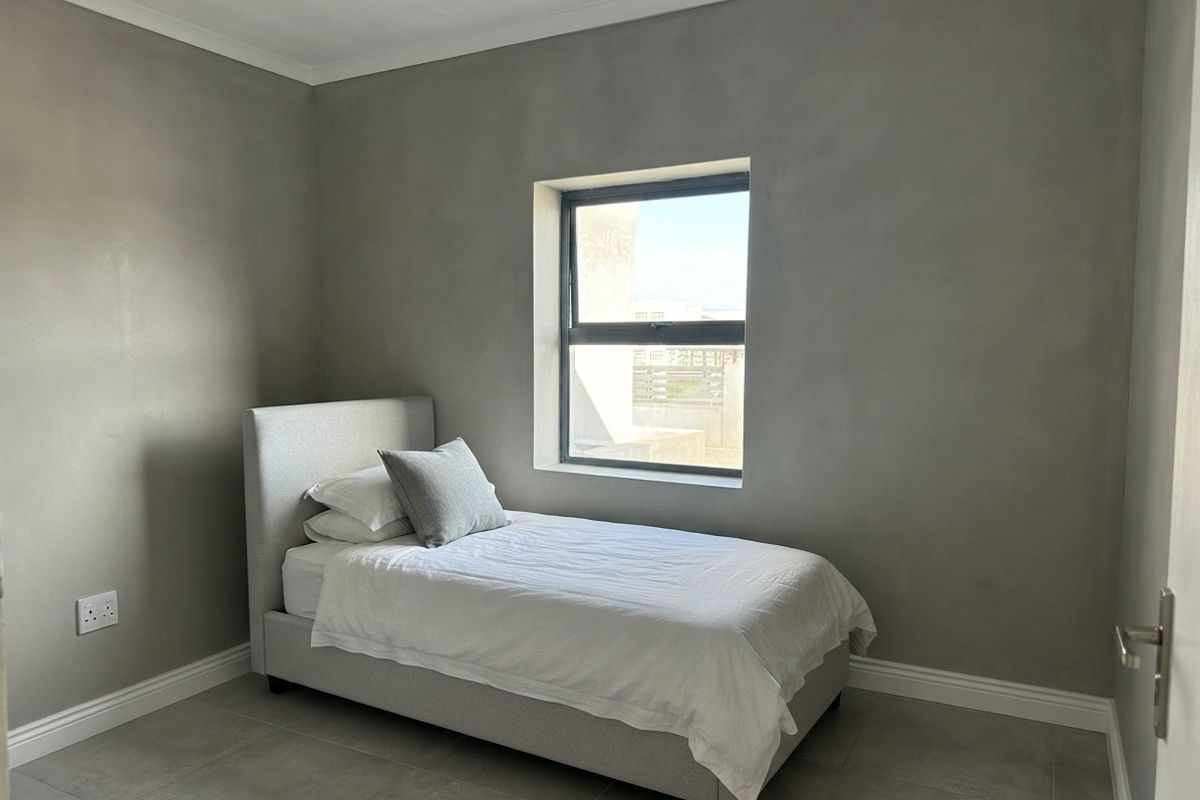 A clean, modern bedroom featuring neutral grey walls, tiled flooring, and a single window providing natural light.