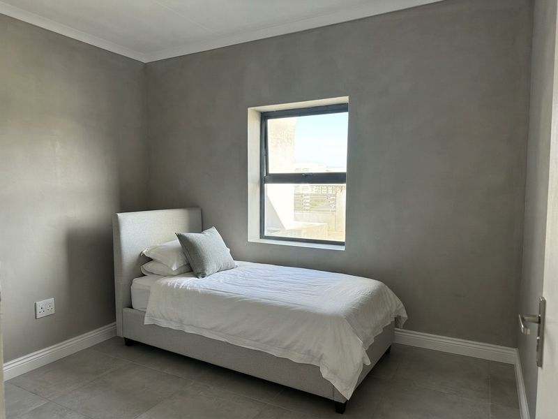 A clean, modern bedroom featuring neutral grey walls, tiled flooring, and a single window providing natural light.