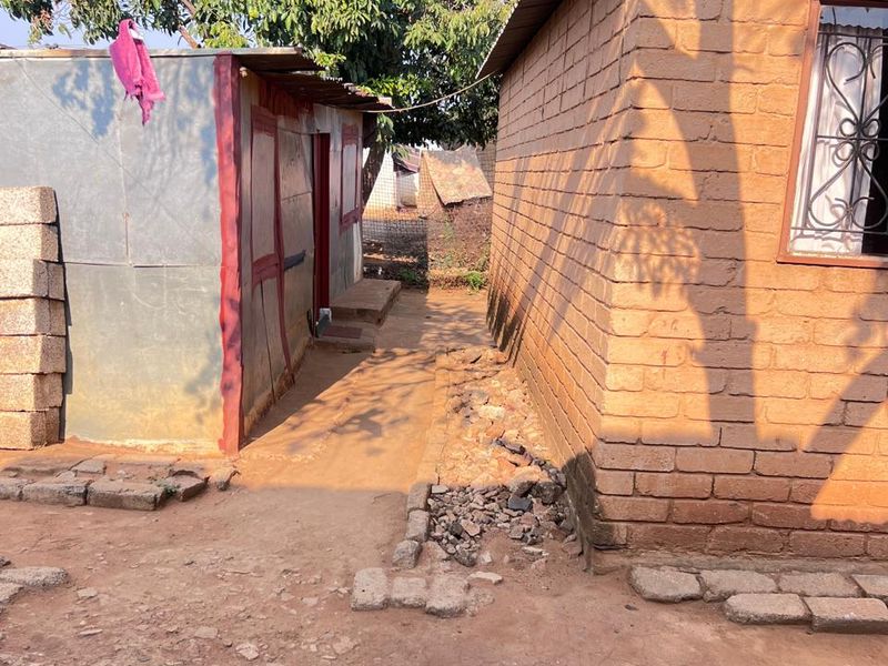 Exterior view showing a brick structure and a secondary corrugated metal outbuilding with an unpaved dirt pathway between them.