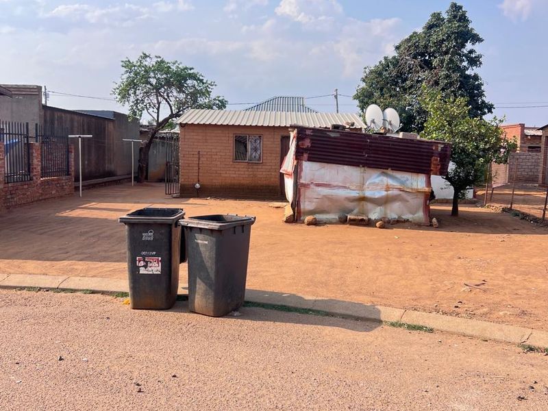 Front view of a residential property featuring a brick structure with a corrugated metal roof and perimeter fencing.