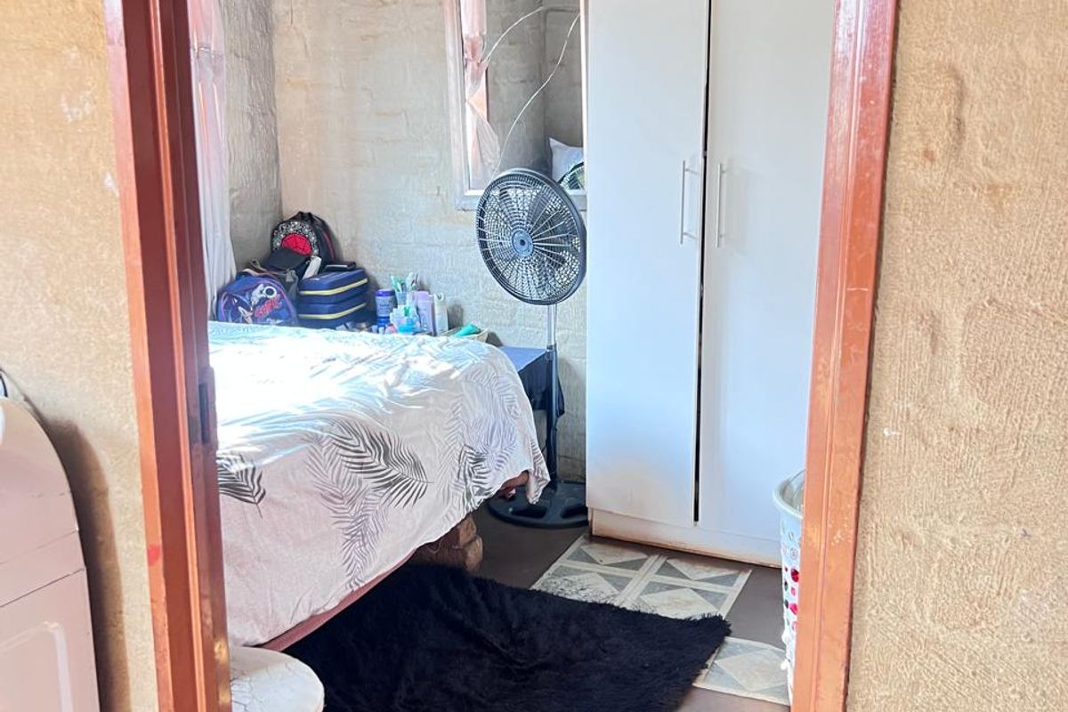 A compact bedroom featuring exposed brick walls, a corrugated metal ceiling, and tiled flooring, offering a basic shell ready for renovation and finishing.
