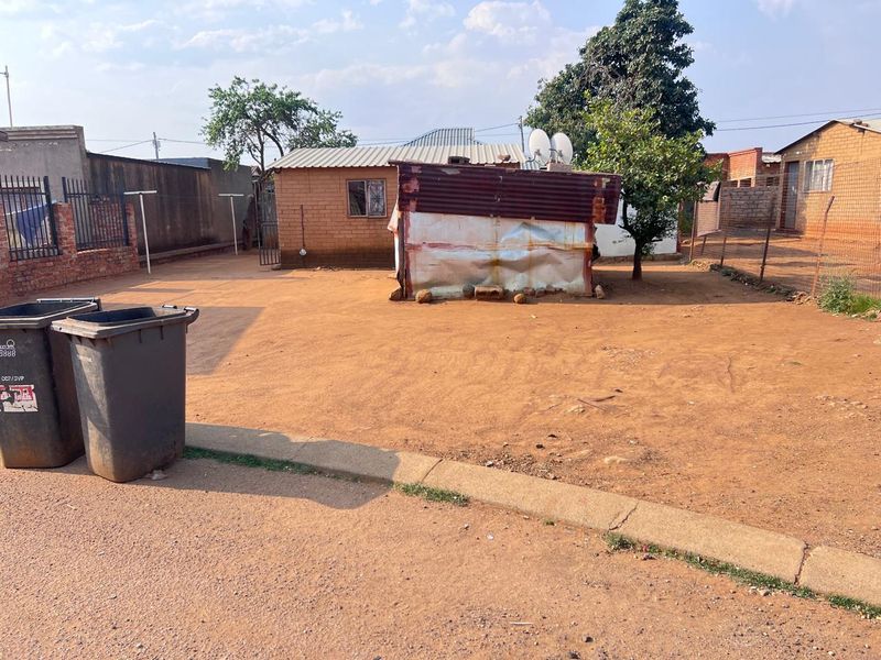 Rear yard area featuring a corrugated iron structure, wire fencing, and a brick boundary wall on an unpaved plot.