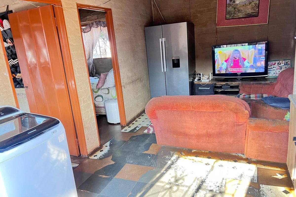 Living area featuring tiled flooring and exposed brick walls, providing a basic layout with direct access to adjacent rooms.