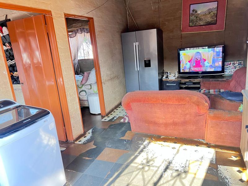Living area featuring tiled flooring and exposed brick walls, providing a basic layout with direct access to adjacent rooms.