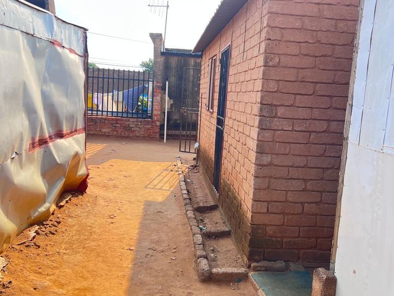 A view of the rear exterior area featuring a brick structure with a metal roof and a fenced perimeter.