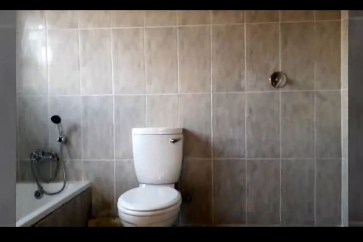 A functional bathroom featuring a bathtub, toilet, and full-height wall tiling, currently in need of cosmetic updates and maintenance.