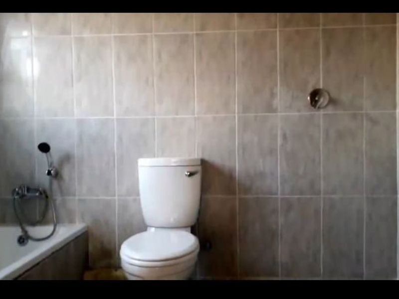 A functional bathroom featuring a bathtub, toilet, and full-height wall tiling, currently in need of cosmetic updates and maintenance.