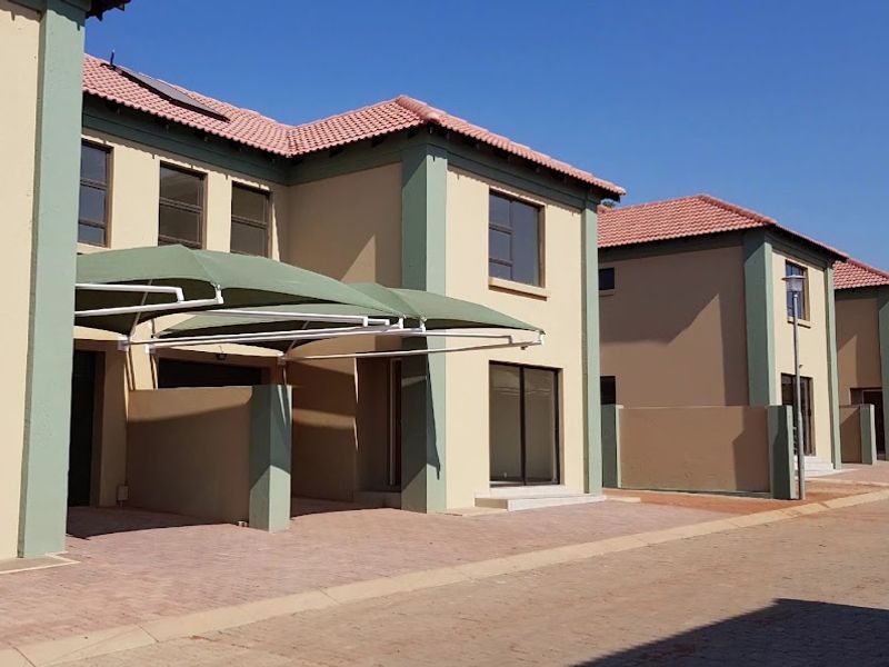 Front elevation of a modern apartment complex featuring paved driveways, shade cloth carports, and tiled roofing with neutral exterior paint.