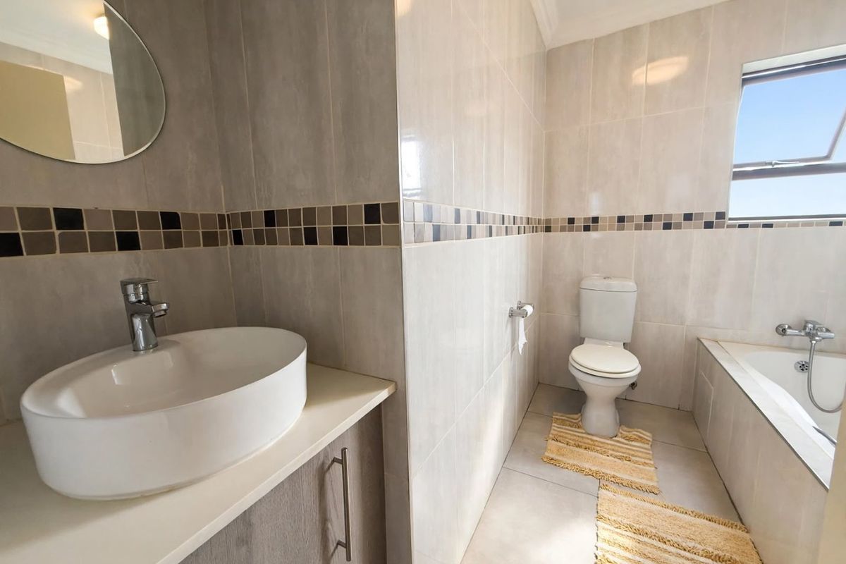 A well-maintained bathroom featuring a modern vessel sink on a vanity cabinet, a built-in bathtub, and neutral wall tiling with a decorative accent border.