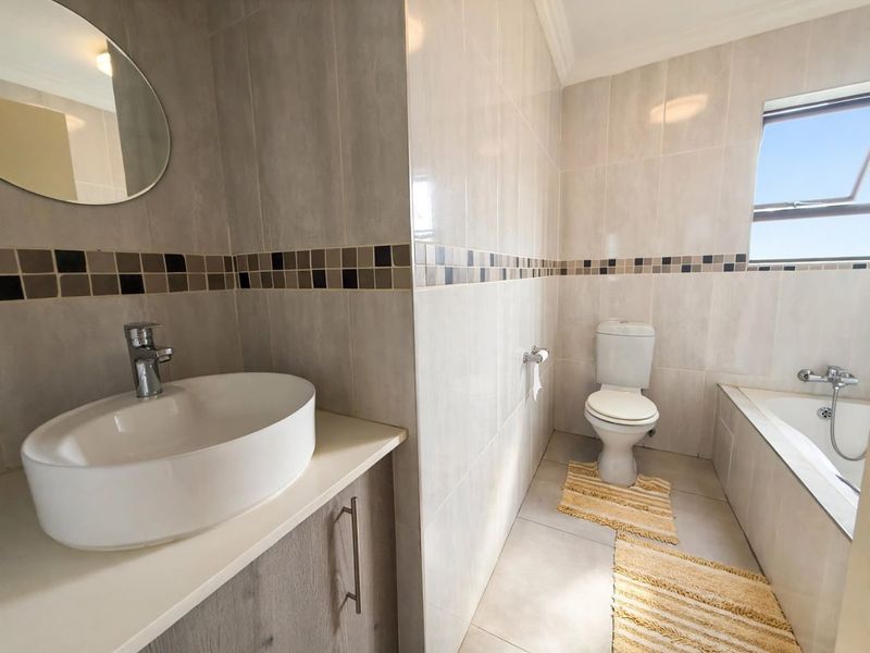 A well-maintained bathroom featuring a modern vessel sink on a vanity cabinet, a built-in bathtub, and neutral wall tiling with a decorative accent border.