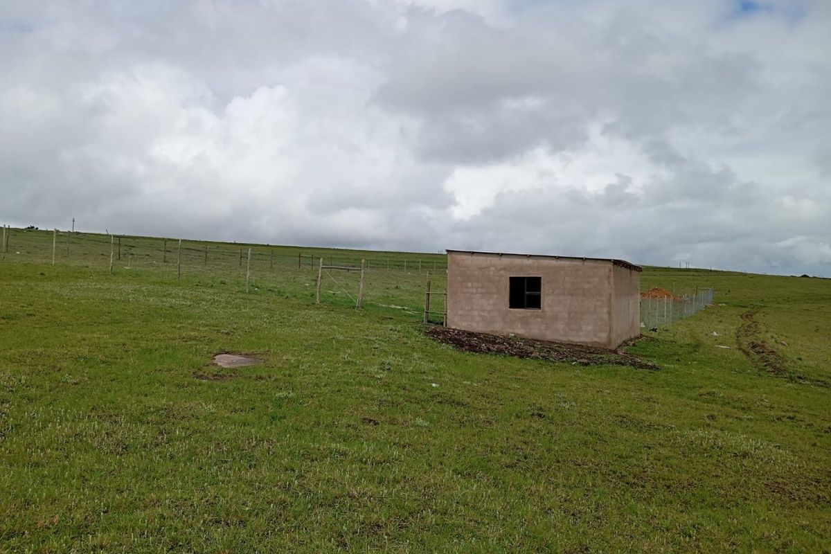 A view of a vacant residential plot featuring a small, unfinished masonry structure and perimeter wire fencing set against an open landscape.