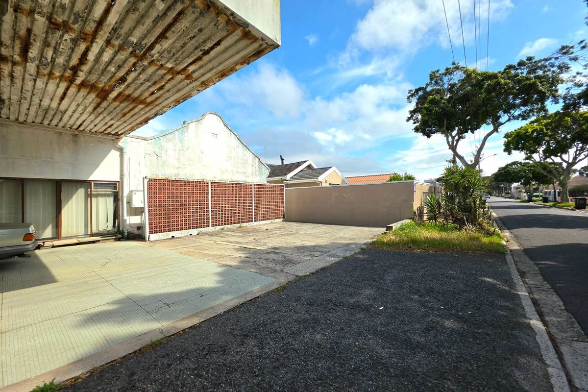 Front exterior view of a commercial property featuring a paved driveway, metal canopy, and breeze block boundary wall.