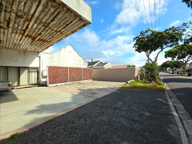 Front exterior view of a commercial property featuring a paved driveway, metal canopy, and breeze block boundary wall.