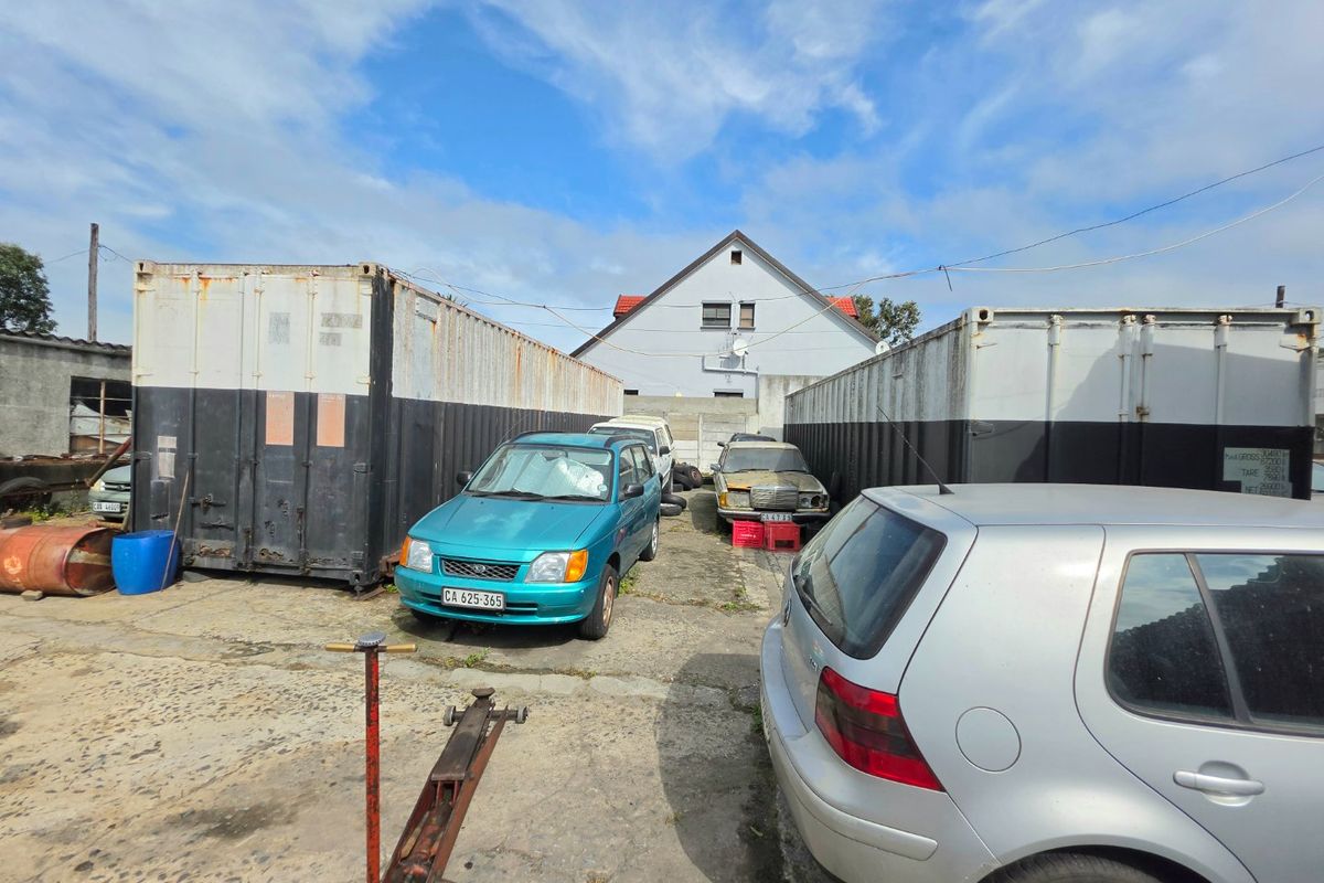 Rear exterior yard area featuring two large shipping containers and concrete paving, currently used for vehicle storage.