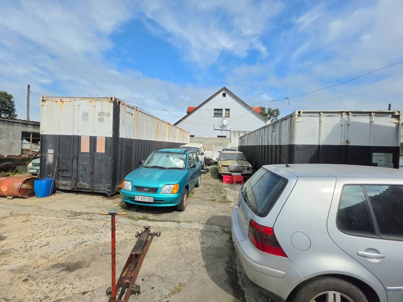 Rear exterior yard area featuring two large shipping containers and concrete paving, currently used for vehicle storage.