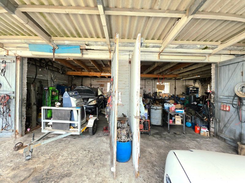 A functional commercial garage space featuring exposed timber beams, corrugated roofing, and concrete flooring, currently utilized for vehicle maintenance and storage.