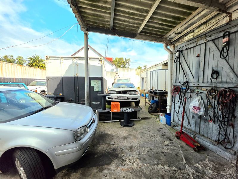 A functional commercial garage space featuring a corrugated roof, concrete flooring, and large timber doors, currently utilized for vehicle storage and maintenance.