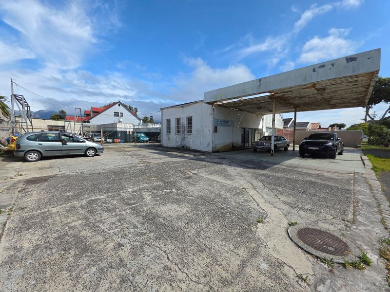 Commercial property featuring a large concrete forecourt, a metal canopy structure, and a single-story building with weathered exterior finishes.