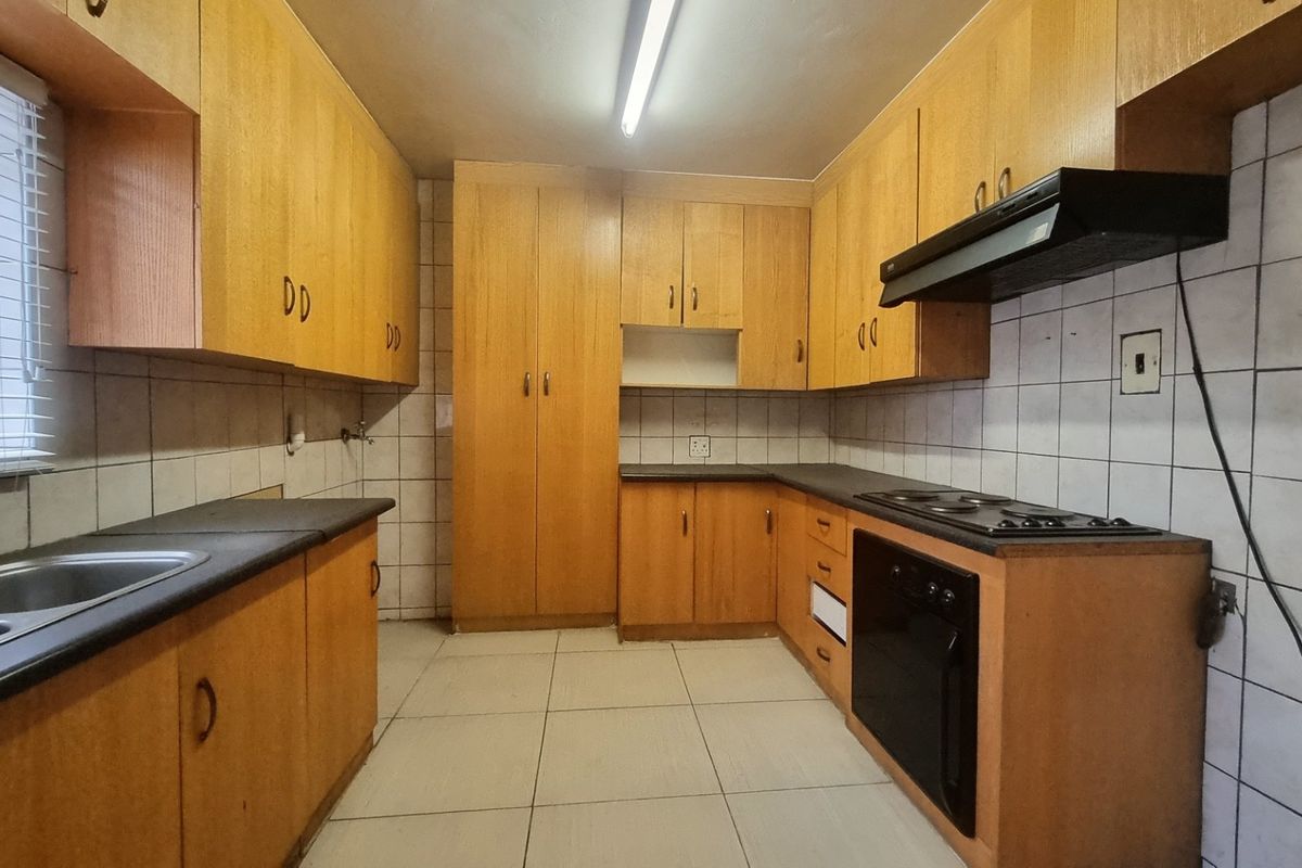 A functional kitchen featuring laminate cabinetry, built-in oven, electric hob, extractor fan, and tiled finishes throughout.