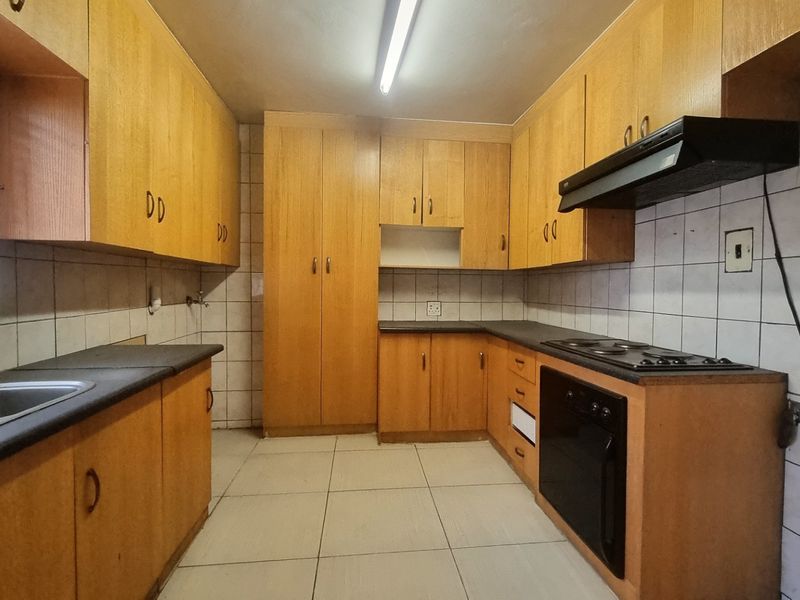 A functional kitchen featuring laminate cabinetry, built-in oven, electric hob, extractor fan, and tiled finishes throughout.