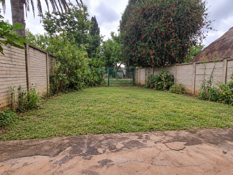 A private rear garden featuring a lawn, established perimeter brick walls, a metal access gate, and a concrete patio area.