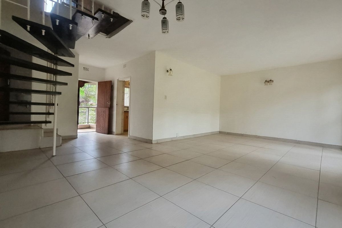 Spacious open-plan living area featuring neutral ceramic floor tiles, a distinctive spiral staircase, and direct access to an outdoor balcony.