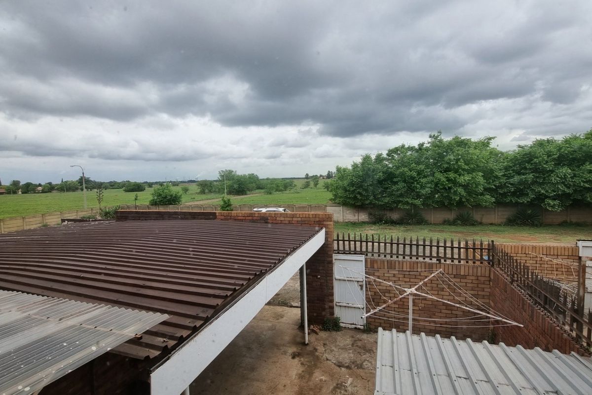 An elevated view of the rear exterior area featuring corrugated metal roofing, brick boundary walls, and open outdoor space with a rural outlook.