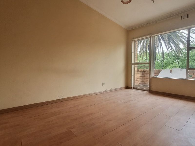 An empty living room featuring laminate flooring, large windows, and a sliding door leading to an outdoor area, offering a blank canvas for renovation.