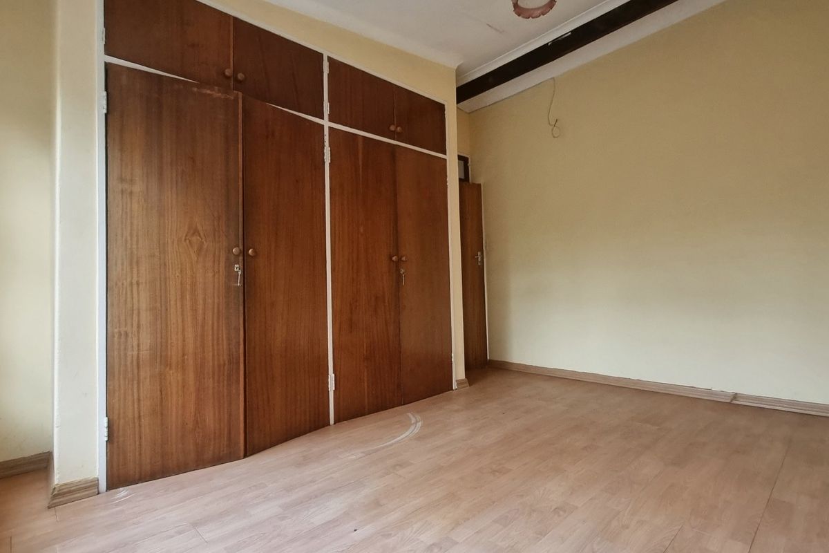 An empty bedroom featuring built-in wooden cupboards and laminate flooring, offering a blank canvas for renovation or restyling.