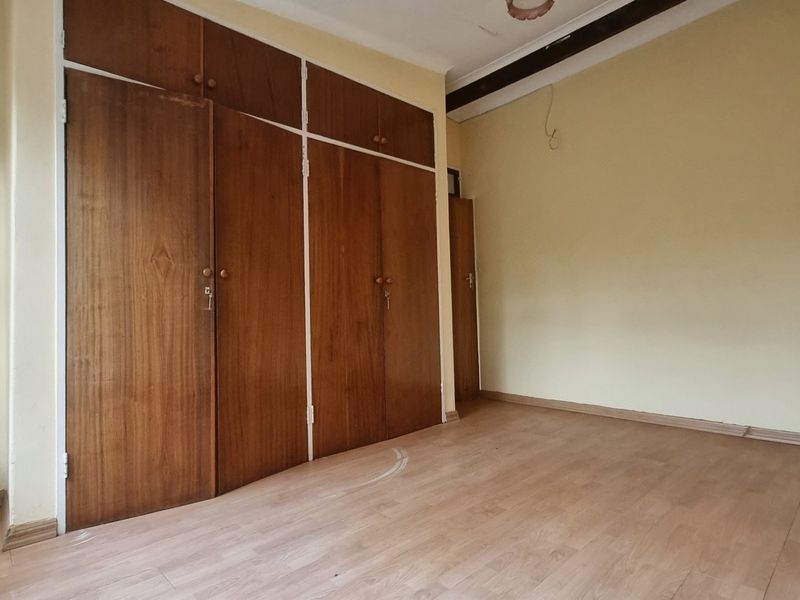An empty bedroom featuring built-in wooden cupboards and laminate flooring, offering a blank canvas for renovation or restyling.