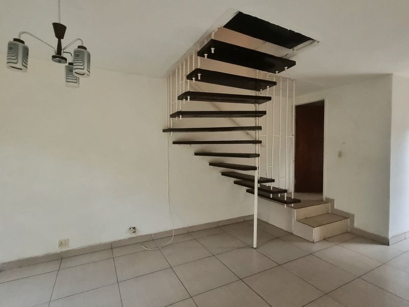 An open-plan living area featuring a distinctive open-tread staircase, tiled flooring, and direct access to the exterior through a sliding glass door.