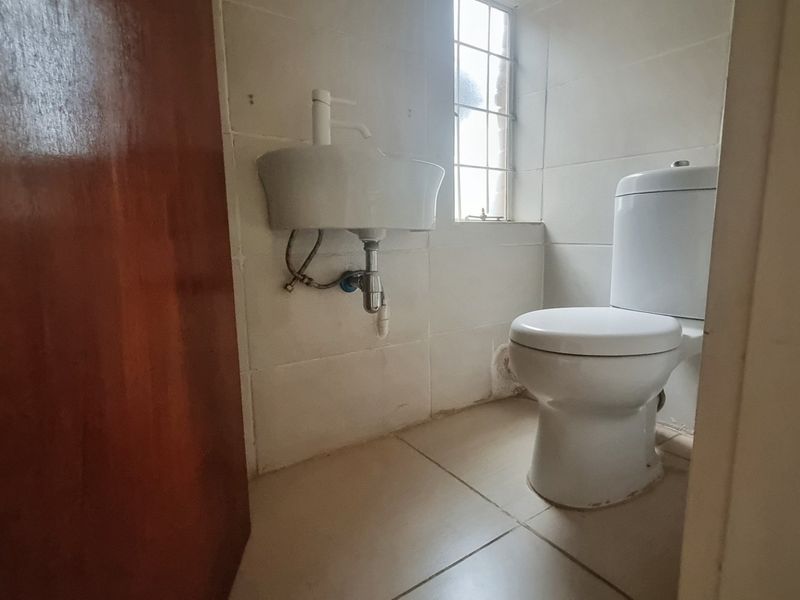 A compact guest bathroom featuring a wall-mounted basin, standard toilet, and tiled finishes, requiring minor cosmetic updates to improve its overall presentation.