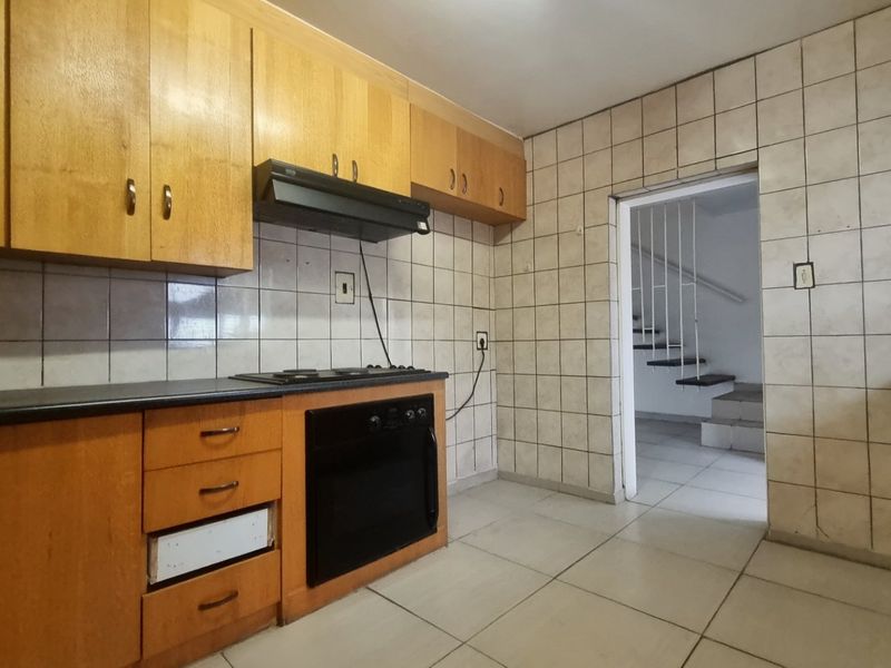 A functional kitchen featuring wooden cabinetry, built-in oven, gas hob, and tiled finishes, offering a blank canvas for modern renovation.