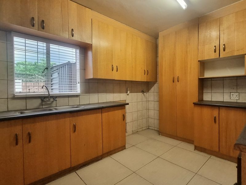 A functional kitchen featuring ample laminate cabinetry, a double basin sink, tiled backsplash, and built-in pantry storage, offering a practical layout for renovation.